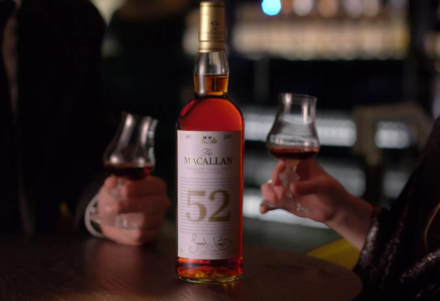 people holding whisky glasses with the macallan 52 years old 2018 release whisky bottle in centre