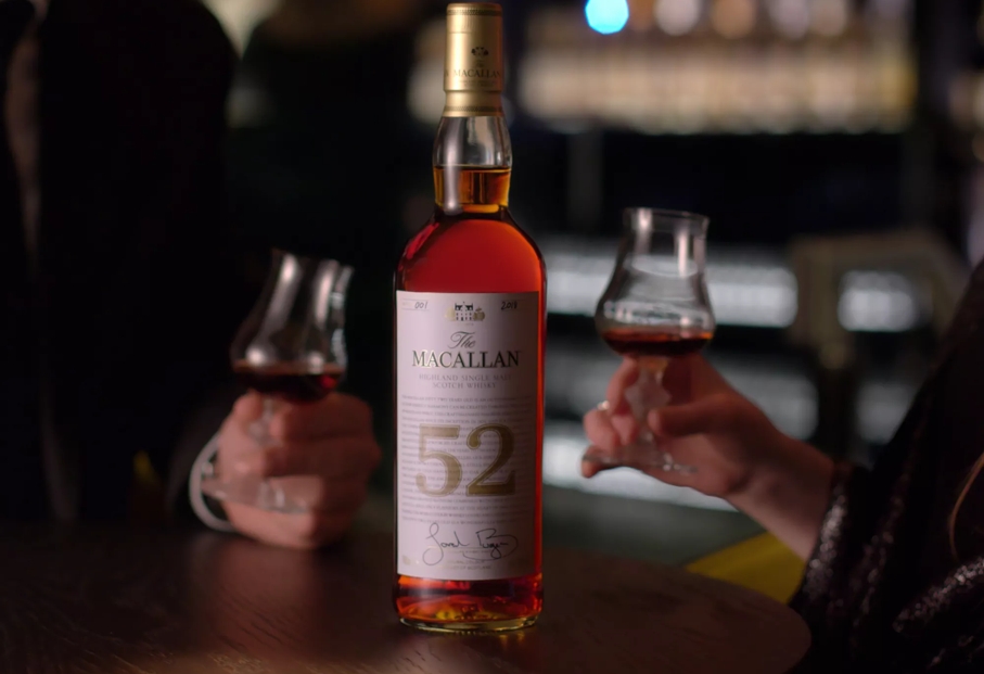people holding whisky glasses with the macallan 52 years old 2018 release whisky bottle in centre