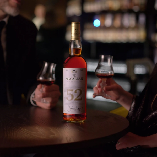 people holding whisky glasses with the macallan 52 years old 2018 release whisky bottle in centre